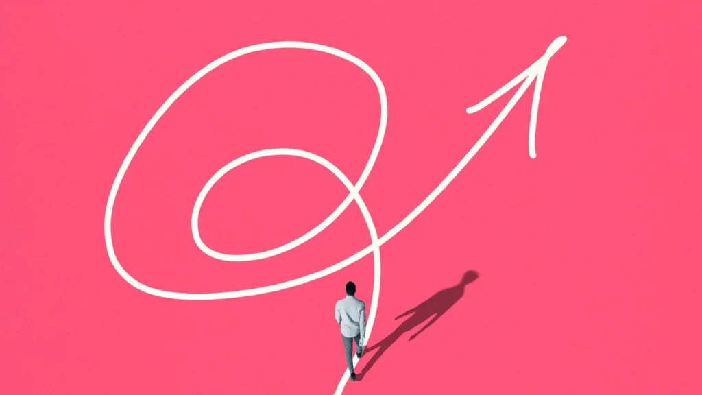 A person walks along a winding white arrow path on a pink background. The arrow spirals and points upwards, symbolizing progress or direction. The persons shadow extends to the right.