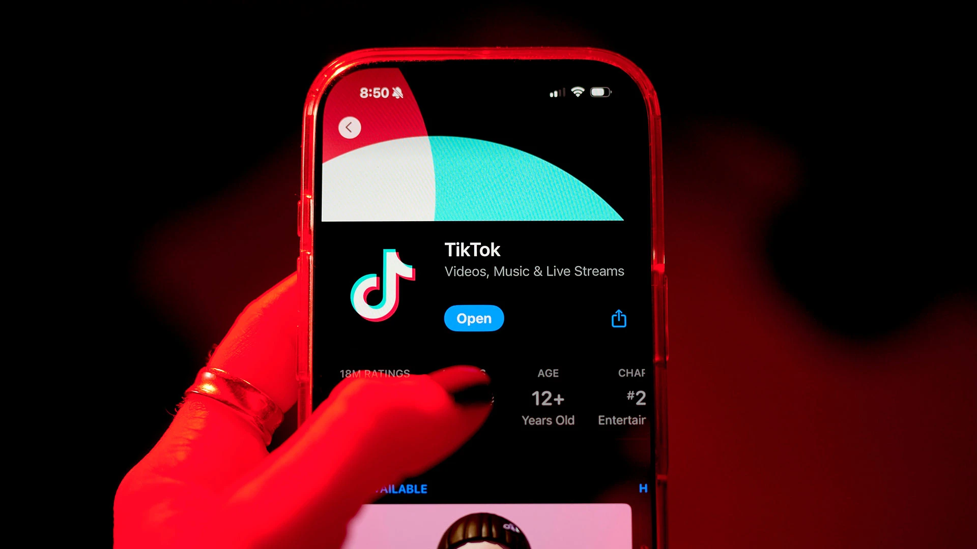 A hand holds a smartphone displaying the TikTok app page on the screen. The app icon and name are visible, with options to open it. The background is red, and the app is rated for ages 12 and up.