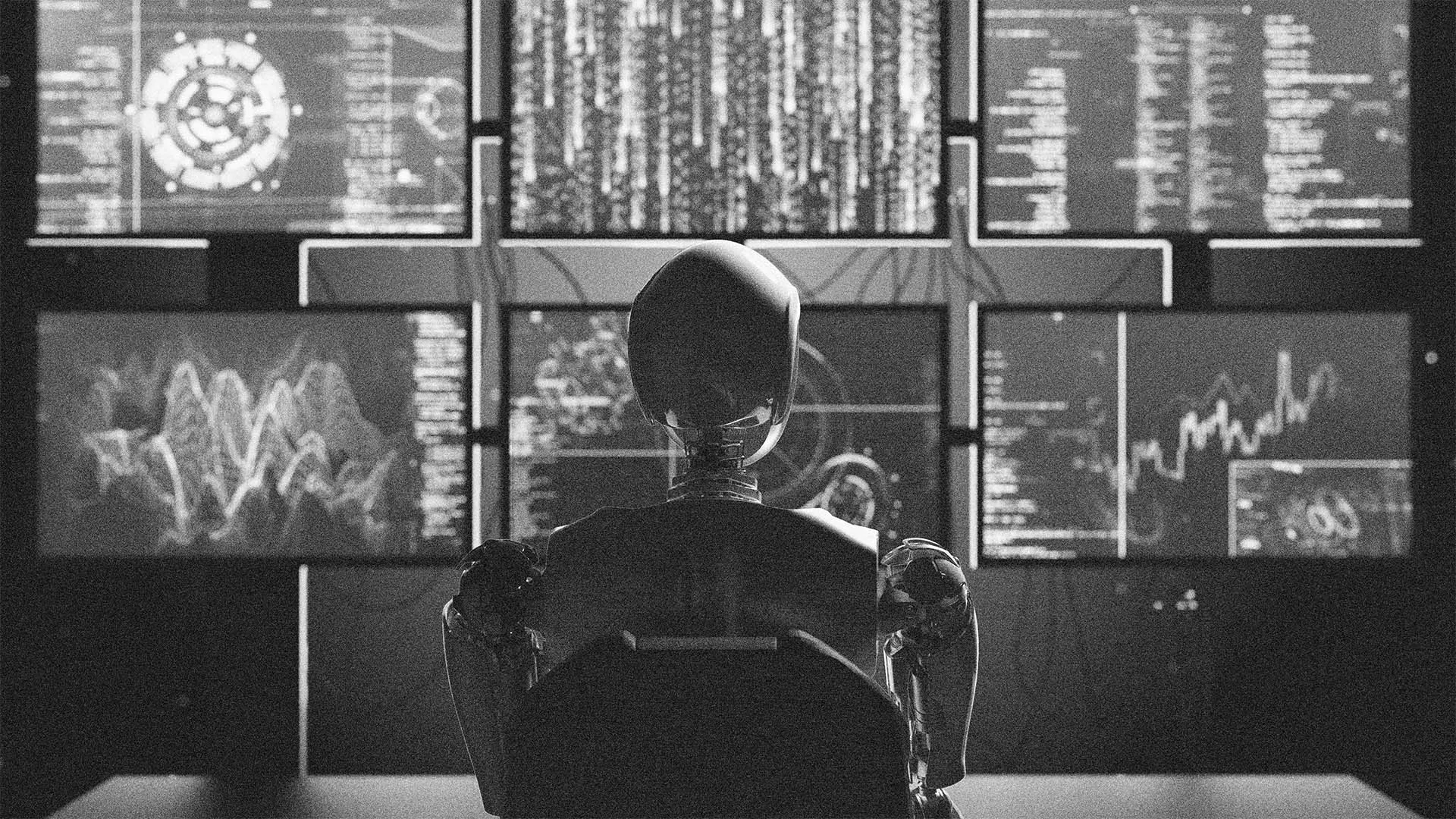 A humanoid robot sits at a desk facing multiple computer screens displaying complex data, graphs, and code, creating a high-tech, futuristic atmosphere. The image is in black and white.